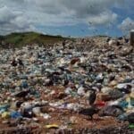 Área de descarte irregular com poluição do solo, mostrando resíduos espalhados, manchas escuras no terreno e sinais de contaminação ambiental.