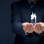 um homem de terno e gravata tem as duas mãos estendidas em forma de concha e dentro delas figuras de pessoas manipuladas pelas Política Climática e governança