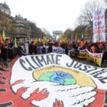 muitas pessoas em evento na rua apresentam uma enorme faixa escrito justiça Climática em inglês e protesta sobre a injustiça.