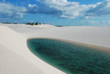 Dunas costeiras sob luz do sol, mostrando areia branca moldada pelo vento.