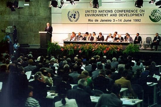 um auditório cheio de pessoas e em cima da plenária uma placa escrita em inglês: conferência nacional do meio ambiente.