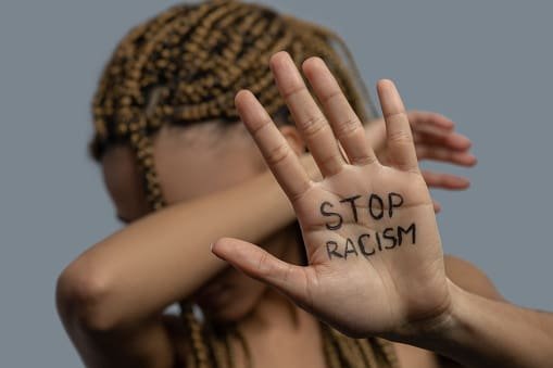 Pare com o racismo. Jovem mulher afro-americana mostrando a palma da mão com a frase: "pare com o racismo", cobrindo o rosto com o cotovelo.