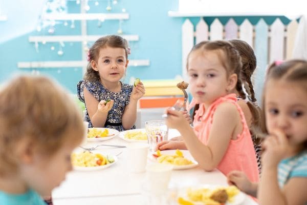 Grupo de crianças sentadas à mesa com o almoço e comendo algo apetitoso e aprendendo sobre educação alimentar