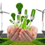 Imagem sobre energia sustentável mostrando mãos segurando lâmpadas ecológicas com textura de plantas, cercadas por painéis solares e turbinas eólicas ao fundo.