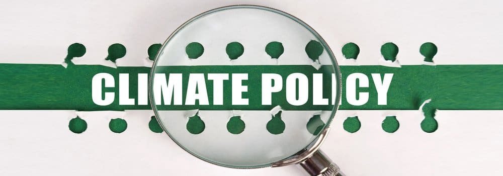 Lupa destacando a frase “Climate Policy” sobre uma faixa verde, simbolizando análise e tomada de decisão em economia e política do clima.