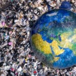 Representação da poluição e impactos ambientais mostrada por um globo terrestre parcialmente coberto por uma grande quantidade de lixo e resíduos espalhados ao redor.