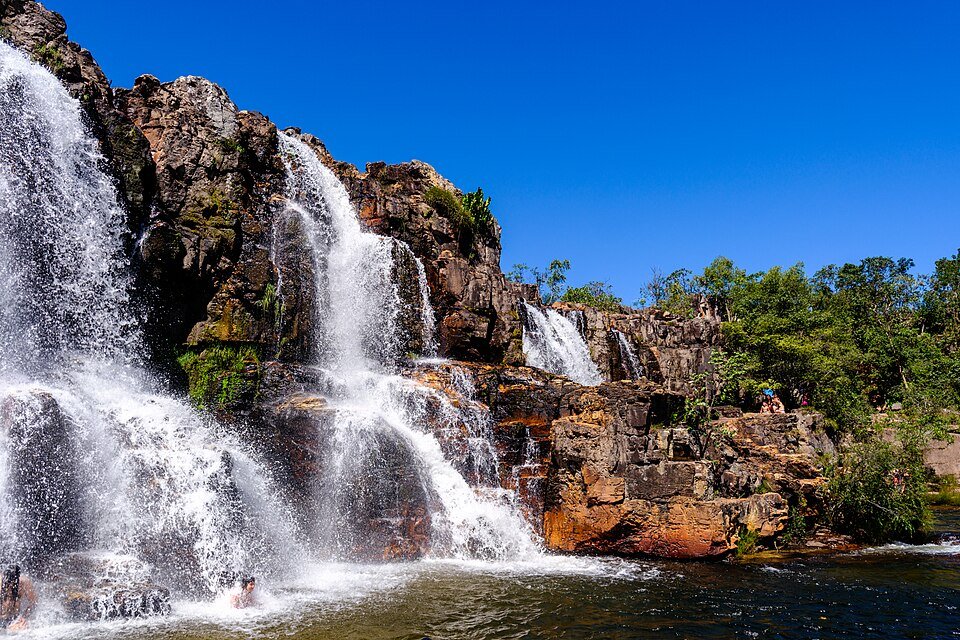 Várias quedas d'água descendo por paredões de rocha avermelhada, sob céu azul, nas Cataratas dos Couros