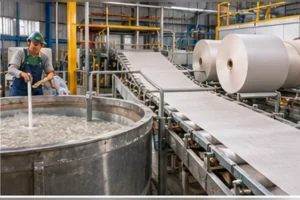 Fábrica de papel com um tanque de pasta de papel, uma esteira onde a pasta vira folha e grandes rolos de papel novo