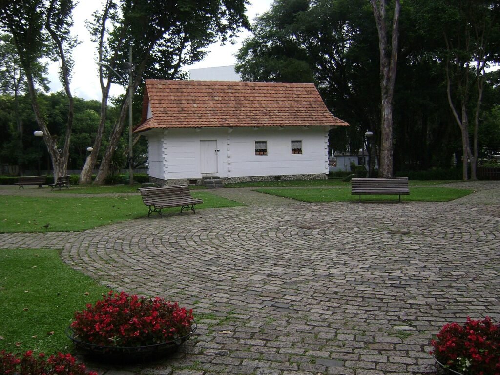 Casa de madeira cercada por árvores e caminho de pedras no Parque Estadual João Paulo II, em Curitiba (PR)