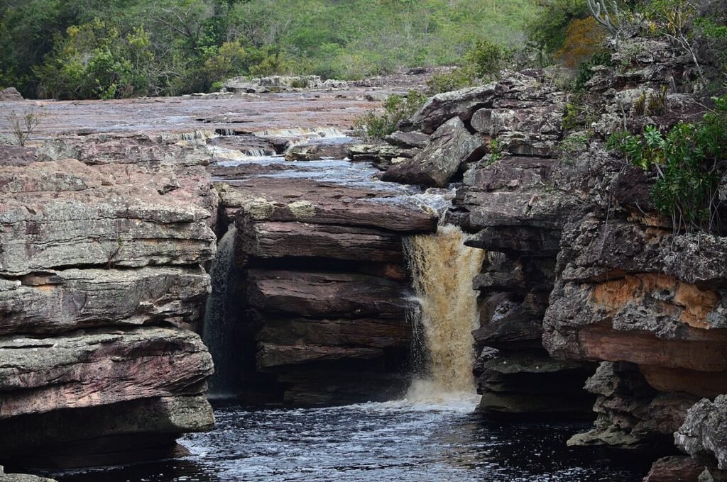 Pequena cachoeira de água escura caindo entre camadas de pedra