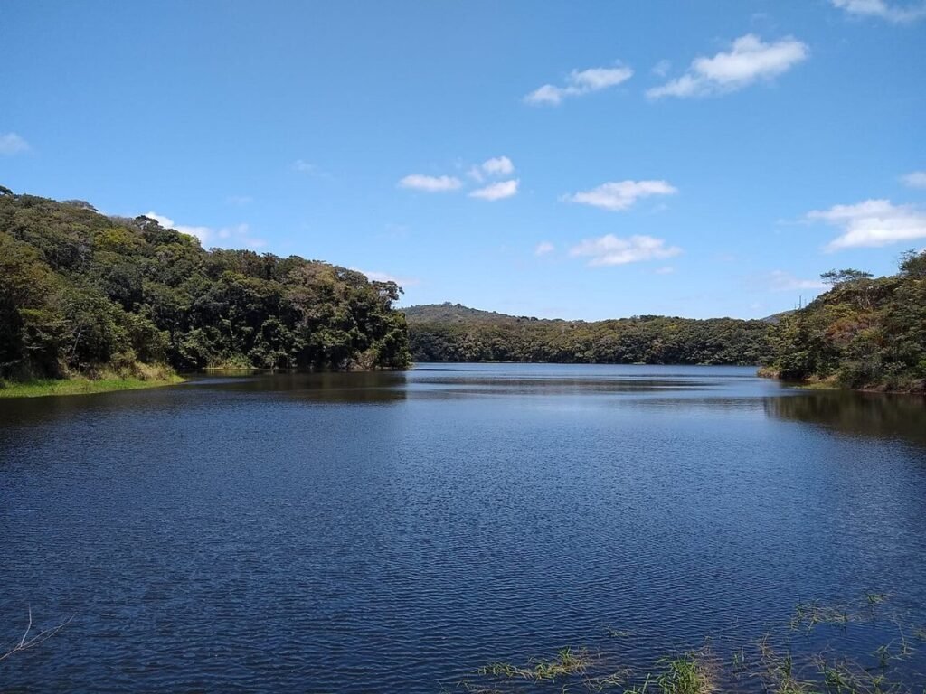 Lago de água azul cercado por morros cobertos de mata, no Parque Natural Municipal Professor João Vasconcelos Sobrinho